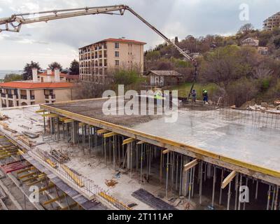 Gießen von Betonzement auf das Dach eines im Bau befindlichen Wohngebäudes mit einer Betonpumpmaschine mit hohem Ausleger zur Versorgung der Mixtur Stockfoto