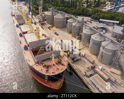 Verladung von Getreide in Laderäume von Seefrachtschiffen im Seehafen aus Getreidesilos. Bunkerung von Trockenfrachtschiffen mit Getreide. Draufsicht aus der Luft Stockfoto