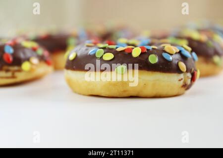 Set aus braunem Schokoladen-Donut, dekoriert mit Smarties isoliert auf weißem Hintergrund, Seitenansicht. Gebratene Teigkonfektion, Dessertessen, süßer Snack mit ch Stockfoto