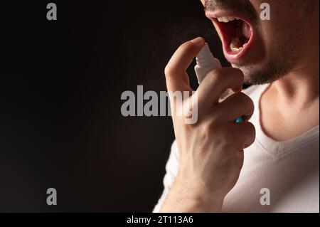 Mann sprüht sich die Kehle aus der Nähe, isoliert auf schwarzem Hintergrund Stockfoto
