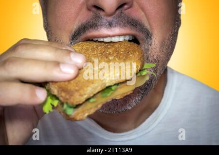 Unwiderstehliches Verlangen nach Junk Food. Nahaufnahme eines hungrigen Mannes, der in einen Käsetoast beißt. Stockfoto