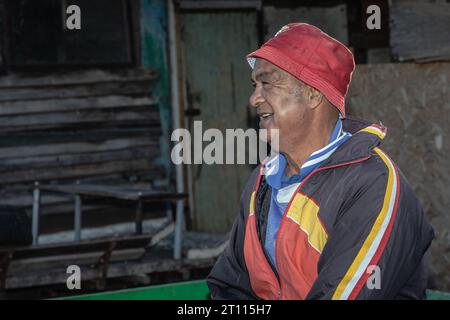 Ein armer, älterer Mann mit gemischter Rasse, lässig gekleidet und mit rotem Hut, Strahlen mit einem warmen und aufrichtigen Lächeln Stockfoto