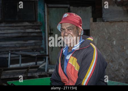 Ein armer, älterer Mann mit gemischter Rasse, lässig gekleidet und mit rotem Hut, Strahlen mit einem warmen und aufrichtigen Lächeln Stockfoto