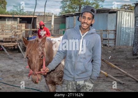 Ein junger Mann mit gemischter Rasse, der neben seinem Wagenpferd stand, der zum Ziehen von Wagen benutzt wurde, um Waren in der armen Gemeinde in Südafrika zu transportieren Stockfoto