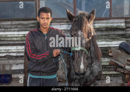 Ein junger Mann mit gemischter Rasse, der neben seinem Wagenpferd stand, der zum Ziehen von Wagen benutzt wurde, um Waren in der armen Gemeinde in Südafrika zu transportieren Stockfoto