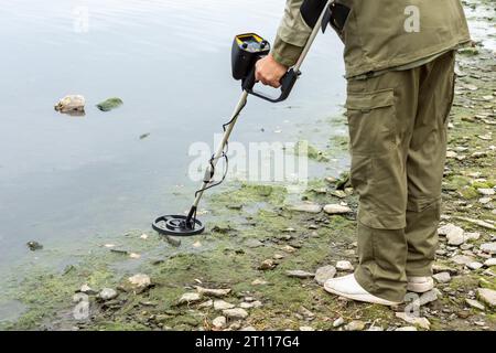 Ein Mann mit einem Metalldetektor am Ufer eines Reservoirs. Metallsuchungen in der Küstenzone. Stockfoto