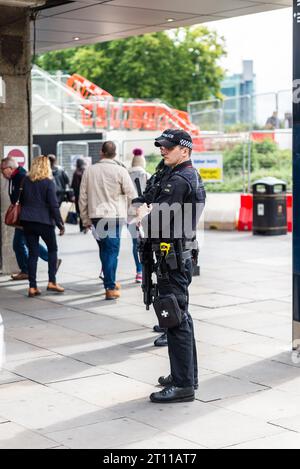 Bewaffnete Polizei in London beobachtet vorbeifahrende Öffentlichkeit vor dem Bahnhof Tower Hill, London, Großbritannien. Autorisierter Feuerwaffenoffizier im Touristengebiet Stockfoto