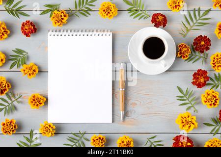 Komposition mit geöffnetem leerem Notizblock und Stift, Tasse schwarzen Kaffee, orangen Blumen und Blätter Ringelblume auf einem blauen Holztisch. Festlicher Bürotisch Stockfoto