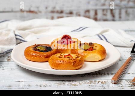 Kleine Pizzasorten. Mini-Pizzen mit Wurst, Gurken, Tomaten, Mozzarella, Petersilie, grün auf einem Teller auf weißem Hintergrund. Nahaufnahme Stockfoto