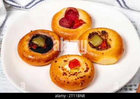 Kleine Pizzasorten. Mini-Pizzen mit Wurst, Gurken, Tomaten, Mozzarella, Petersilie, grün auf einem Teller auf weißem Hintergrund. Nahaufnahme Stockfoto