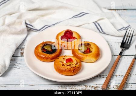 Kleine Pizzasorten. Mini-Pizzen mit Wurst, Gurken, Tomaten, Mozzarella, Petersilie, grün auf einem Teller auf weißem Hintergrund Stockfoto