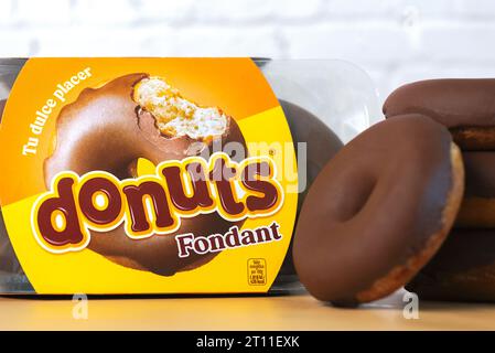 Nahaufnahme einer Schachtel Fondant Chocolate Donuts neben leckeren Donuts auf einem Holztisch. Illustrativer Leitartikel Stockfoto