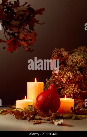 Stillleben mit Kürbis, ausgetrockneten Blättern und brennenden Kerzen. Im Hintergrund getrocknete Hortensienblüten und Eichenzweige. Herbstkonzept. Stockfoto