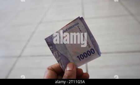 Batu City, Ost-Java, Indonesien. 20. Oktober ,2023: Ein Mann hält indonesisches Geld in zehntausend Rupien Stockfoto