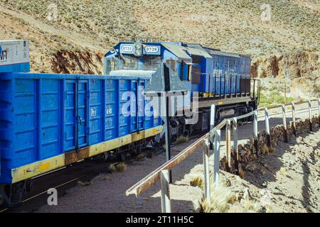 Elektrischer blauer Zug, der durch die Eisenbahn manövriert, umgeben von malerischen Bergen Stockfoto