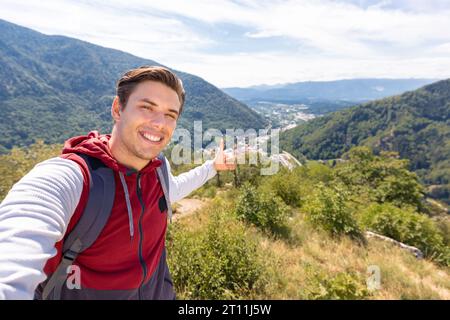 Ein lächelnder Mann macht ein Selfie-Video, spricht und zeigt auf die Schönheit der Natur, Bergpanorama im Hintergrund Stockfoto