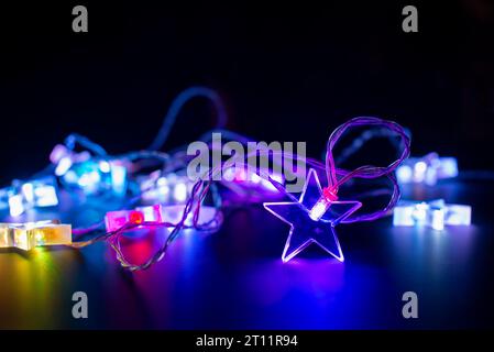 Nahaufnahme von rosa und lila elektrischen weihnachtsschnur Lichtergirlande in Form von Sternen, modernes Ferienhaus Dekor auf schwarzem Hintergrund Stockfoto