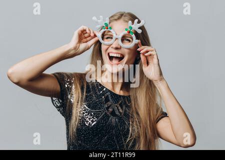 Eine junge lächelnde blonde Frau in Brille mit Hirschgeweih isoliert auf weißem Hintergrund. Weihnachts- und Neujahrskonzept. Stockfoto