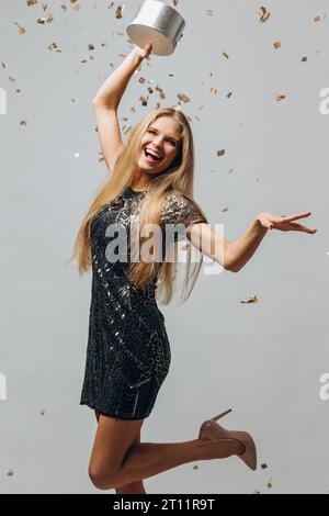 Frohe Weihnachten: Eine glückliche blonde Frau in einem festlichen Kleid hält Weihnachtsgeschenke mit Konfetti Fliegen überall, ein Porträt - Stockfoto. Stockfoto