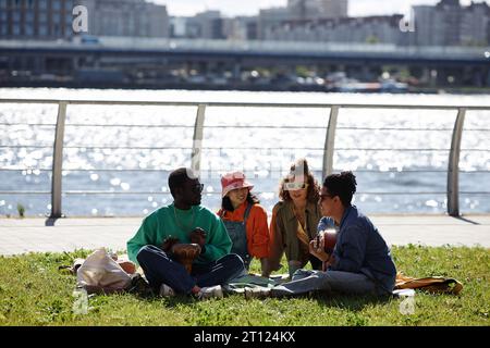 Weitwinkelansicht junger Menschen, die im Freien ein Picknick auf Rasen genießen, mit Skyline im Hintergrund, Kopierraum Stockfoto