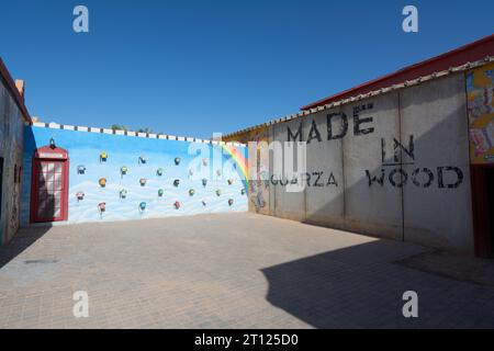 Ouarzazate, Marokko - 10. Oktober 2023: Regenbogenmalte Wand und eine englische Telefonzelle und viele alte Telefone hangen in verschiedenen Farben am Atlas Stockfoto