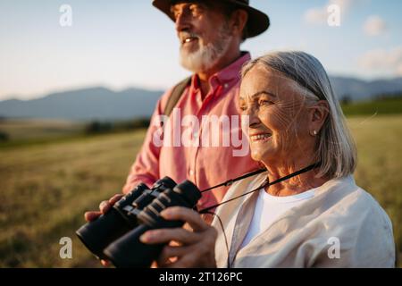 Porträt einer älteren Frau, die durch ein Fernglas schaut. Ältere Ehepartner gehen Pilzpflücken. Stockfoto