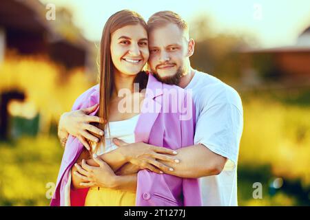 Ehemann umarmt lächelnde Frau, steht hinter ihr, Sommerfamilien-Porträt in der Natur. Stockfoto