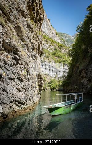 Ein langes, dünnes Ausflugsboot, das an einer steilen Felswände im River Shala Resort im Komani-See, Albanien, verankert ist Stockfoto