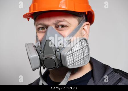 Ein Mann mit Schutzhelm und Atemschutzmaske zum Schutz vor Staub und Gasen auf weißem Hintergrund. Stockfoto