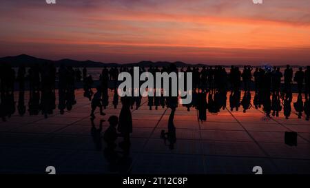 Die Menschenmassen versammeln sich bei Sonnenuntergang um einen Solosaxophonisten, der sich in den Sonnenkollektoren der Begrüßung zur Sonneninstallation bei Sonnenuntergang in zadar kroatien spiegelt Stockfoto