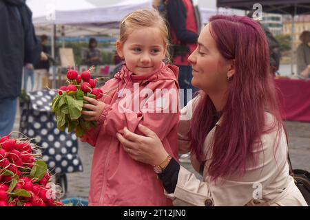 Ein kleines Mädchen mit frischen Radishies und ihrer jungen Mutter auf dem Bauernmarkt in Prag. Stockfoto