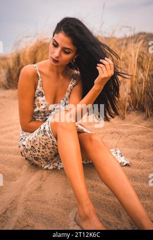 Weißliche Brünette streichelte ihr Haar in einem weißen Blumenkleid am Strand von Cabo de Gata, Nijar. Andalusien, Spanien Stockfoto