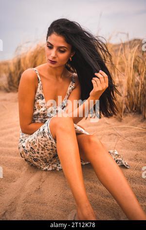 Weißliche Brünette streichelte ihr Haar in einem weißen Blumenkleid am Strand von Cabo de Gata, Nijar. Andalusien, Spanien Stockfoto