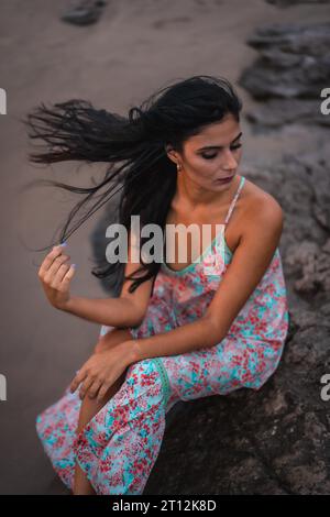 Weißliche Brünette in einem weißen Stoffkleid mit Blumen, am Strand genießen Sie den Urlaub am Meer, vertikales Foto Stockfoto