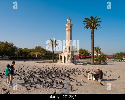 Izmir, Türkei. 5. Oktober 2023. Uhrenturm von Izmir. Taubenfutterverkäufer und Kinder, die mit Tauben spielen. Herbst in Izmir Stockfoto