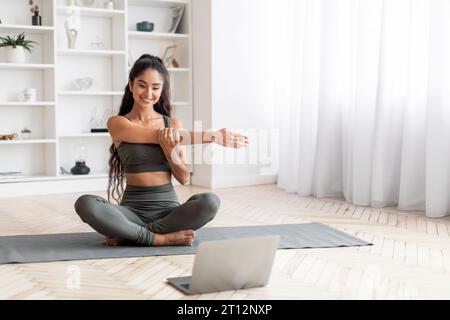 Fitness-Enthusiast Junge indische Frau nimmt an Home Laptop Workout Teil Stockfoto