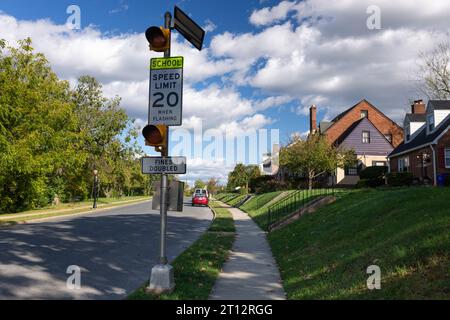 Eine ruhige Vorstadtstraße in Frederick, MD, mit zweistöckigen Häusern, grünen Rasenflächen und einem Warnschild für die Schulzone, das bei 20 km/h blinkt Stockfoto