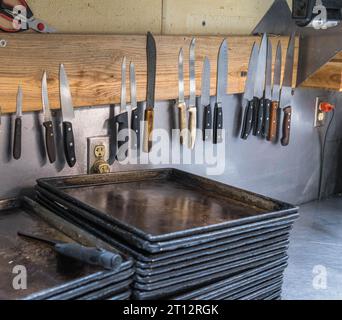 Metallkochen, Backbleche und Messer unterschiedlicher Größe in der Küche eines Pizzaladen in Monroeville, Pennsylvania, USA Stockfoto