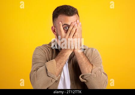 Schockierter tausendjähriger europäer, bedeckt Gesicht mit Händen, Blick von den Fingern Stockfoto
