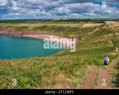 Wanderer auf dem Küstenweg nähern sich dem roten Sand des einsamen Swanlake Beach in Pembrokeshire, Wales, Großbritannien. An einem sonnigen Sommertag mit einem turq aufgenommen Stockfoto