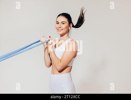 Lächelnde Frau, die Bizepscurl mit Widerstandsband an der weißen Wand macht Stockfoto