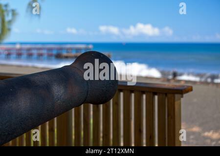 Alte Kanone mit im Hintergrund, die Débarcadère de Saint-Paul (Landung von Saint-Paul) mit den Wellen der Sommersonnenwende. Stockfoto