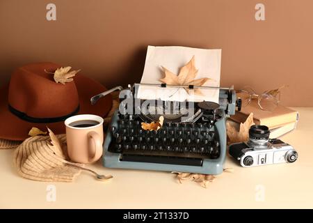 Vintage Schreibmaschine, Hut, Bücher, Fotokamera, Tasse Kaffee, Brille und Herbstblätter auf braunem Hintergrund Stockfoto