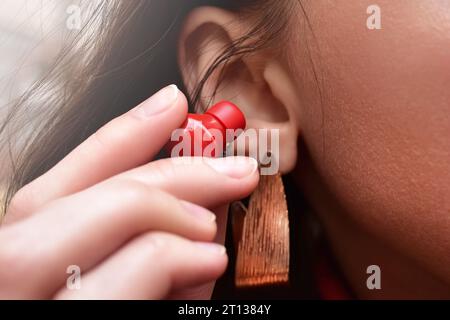 Eine Frau hält einen roten, kabellosen Kopfhörer in der Hand und bringt ihn näher an ihr Ohr, um Musik zu hören. Nahansicht Stockfoto