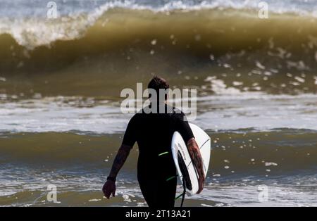 Gilgo Beach, New York, USA - 3. September 2023: Rückansicht eines männlichen Surfers, der einen schwarzen Neoprenanzug trägt und sein Surfbrett mit großem W Stockfoto