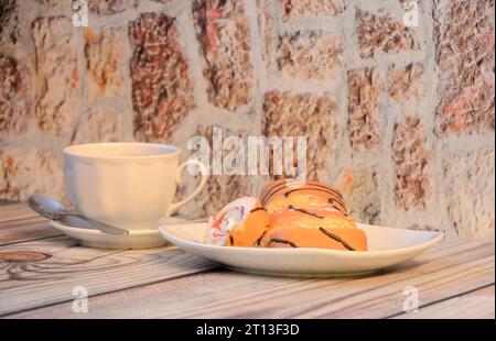 Ein Teller mit frischen Keksbrötchen mit Proteincreme und einer Tasse heißem Tee auf einem Holztisch. Nahaufnahme. Stockfoto