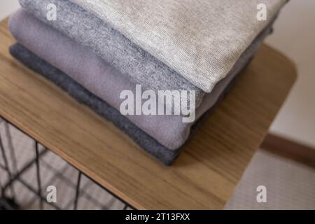 Ein Stapel sauberer, frisch gewaschener, grauer, ordentlich gefalteter Damenbekleidung auf einem Holztisch. Ein Haufen Hemden, Kleider und Pullover auf dem Tisch. Stockfoto