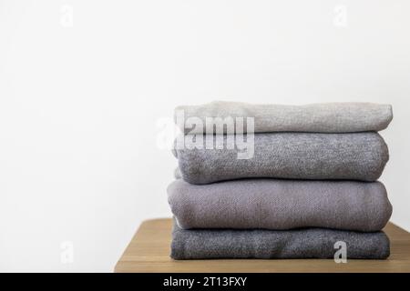 Ein Stapel sauberer, frisch gewaschener, grauer, ordentlich gefalteter Damenbekleidung auf einem Holztisch. Ein Haufen Hemden, Kleider und Pullover auf dem Tisch. Stockfoto