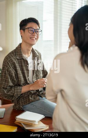 Ein glücklicher und kluger junger asiatischer Mann mit Brille spricht gern und teilt seine Ideen mit einer Freundin im Zimmer. Teamwork, Freundschaft, Hengst Stockfoto