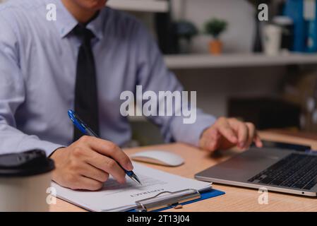Professioneller Geschäftsmann, der mit Laptop an Vertragsunterlagen arbeitet oder Dokumente unterschreibt, Mitarbeiter im Vertragsverhältnis, Investmentfinanzierung und Bankwesen. Stockfoto
